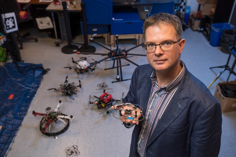 Bert Tanner is pictured in his laboratory. He is holding a tiny drone, and several drones surround him.