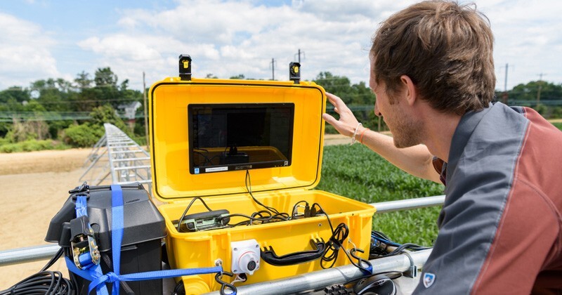 Adam Stager, doctoral student in mechanical engineering, monitors crop data from atop the irrigation system in the outdoor lab at UD’s Newark farm during the summer.