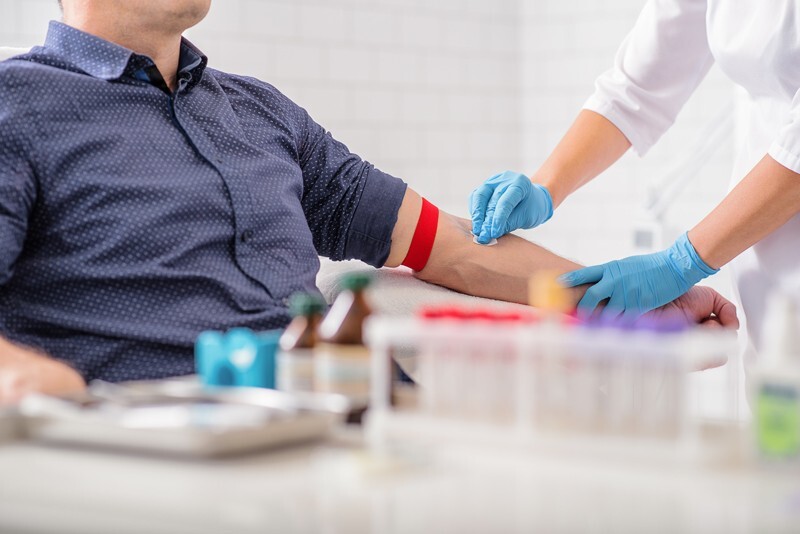 Male person seated while a technician prepares to draw blood.