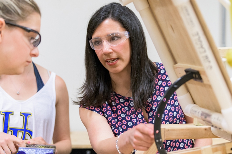 Close-up of a female faculty member explaining a wooden device to a student