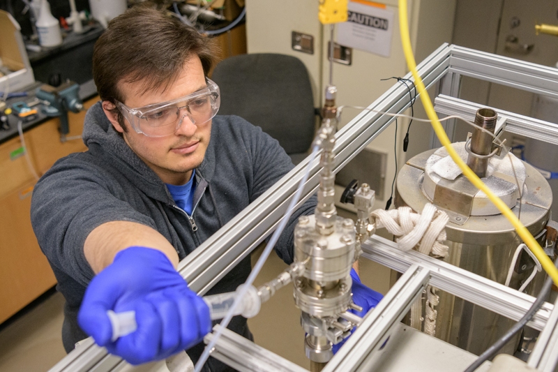 a male graduate student uses a syringe to add fluid to a device