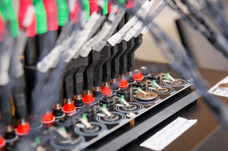 A potentiostat (aka a big box with cables) is attached to a coin cell battery holder, supplying current for electrochemical testing.
