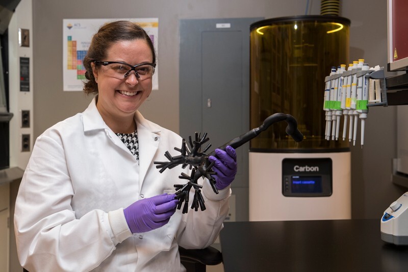 Assistant Professor Catherine Fromen in a lab jacket holding a 3D printed sample of a pulmonary system used in testing.