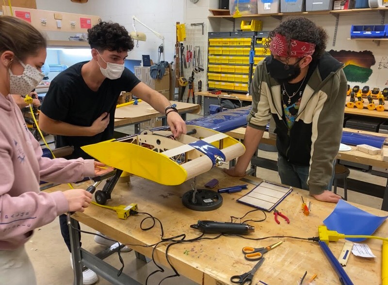 Three students in a workshop assemble a part of a model airplane wing.
