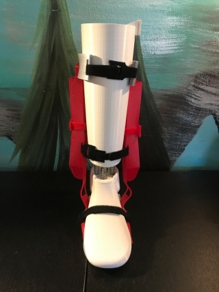 A robotic orthotic device worn like a boot. there are black straps that wrap around the foot and lower leg and red supports on the left and right.