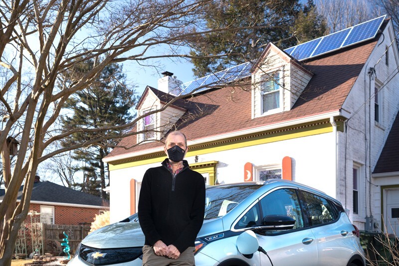 Professor Jeremy Firestone of UD’s School of Marine Science and Policy stands in the driveway of a house with solar panels and an electric vehicle.