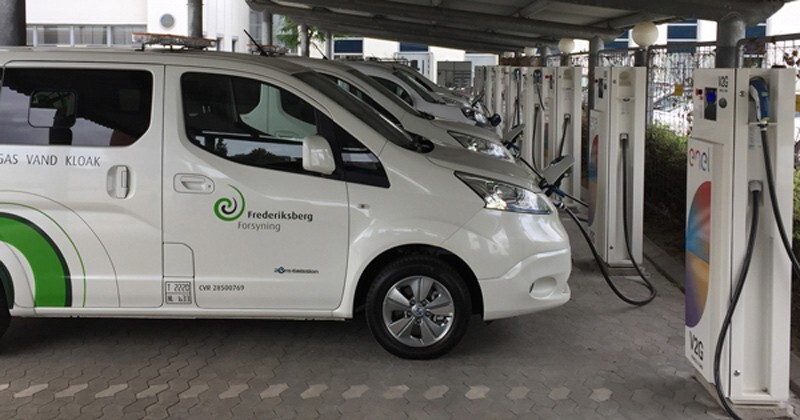 Row of white vans in front of electric charging stations.