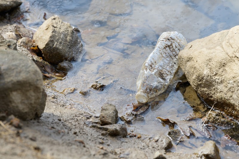 A plastic water bottle partially submerged on the bank of a creek surrounded by rocks.