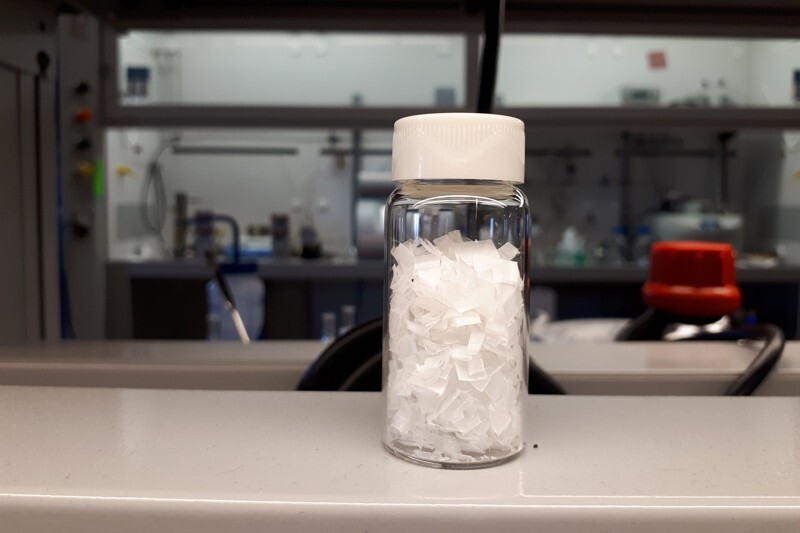A glass bottle containing white, cut-up pieces of plastic.