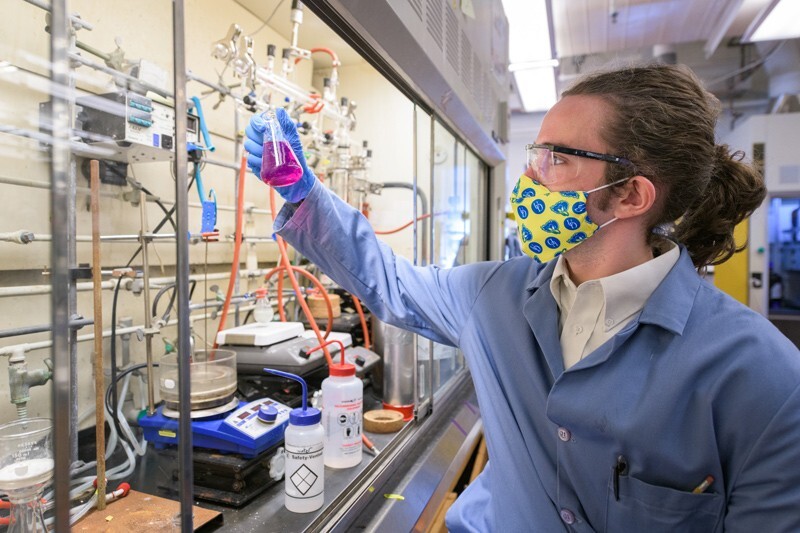 Jackson Burn holding a glass flask full of purple liquid in a lab.