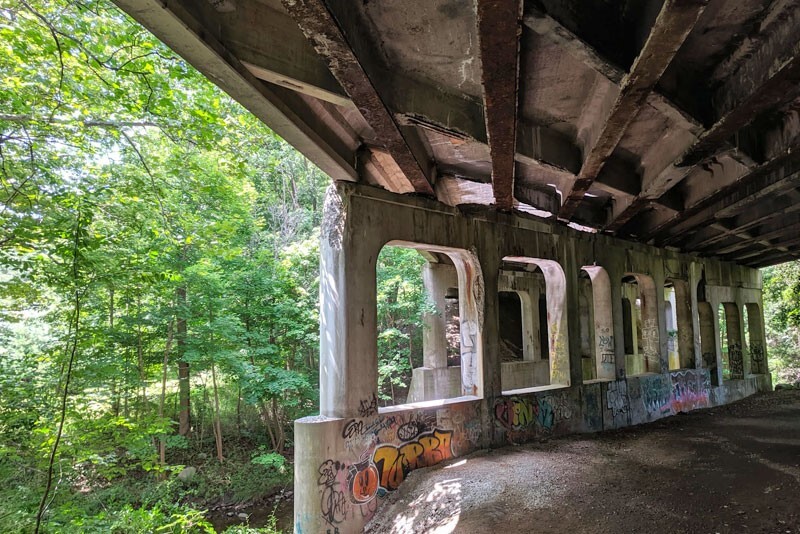 The underside of a concrete bridge showing damaged concrete and graffiti.