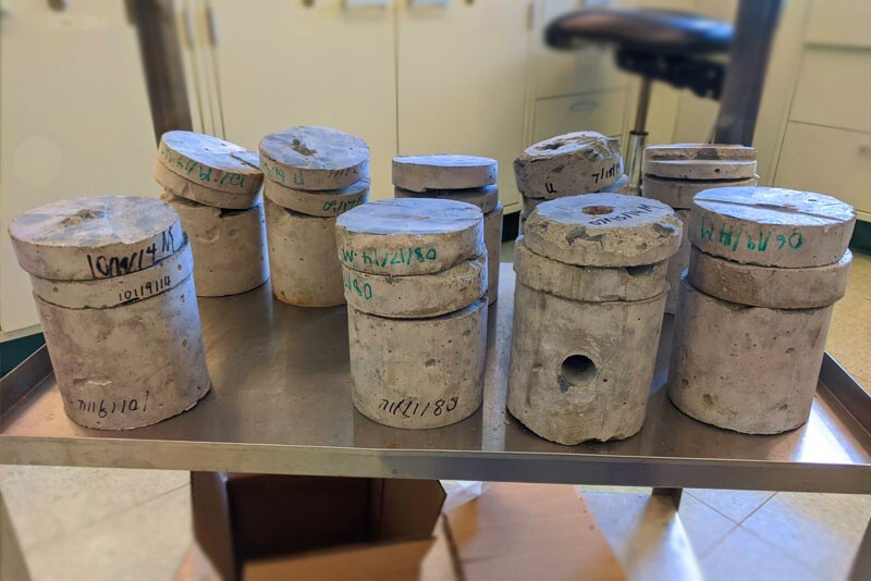 A stainless steel table contains 9 concrete cylinders that have been cut or bored into for testing bacteria.