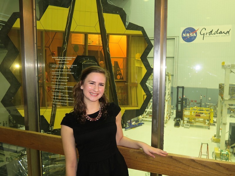 Elaine Stewart is standing outside the cleanroom where the telescope’s mirrors were housed. The main mirror assembly is visible behind her.