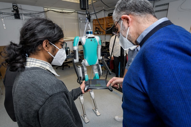 mechanical engineering graduate student Abhijeet Kulkarni (left) and Mechanical Engineering Professor Ioannis Poulakakis look at the controller for the high-tech robot named Digit.