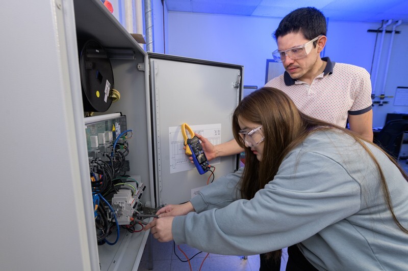 Tasha Kaewnukultorn and Sergio Sepúlveda using a hand-held voltage meter to analyze the output of an electrical inverter.