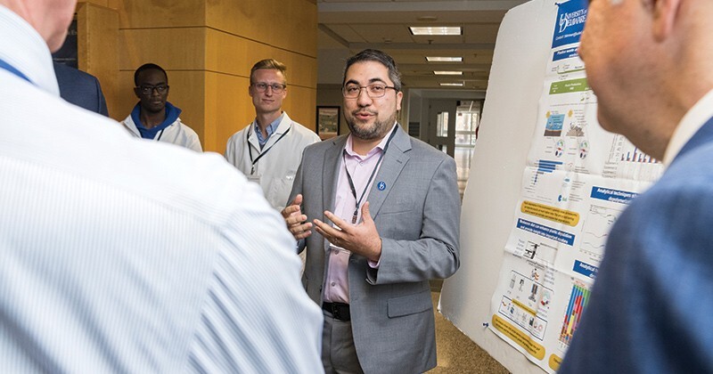 Associate professor Mark Blenner stands in front of a presentation surrounded by people.