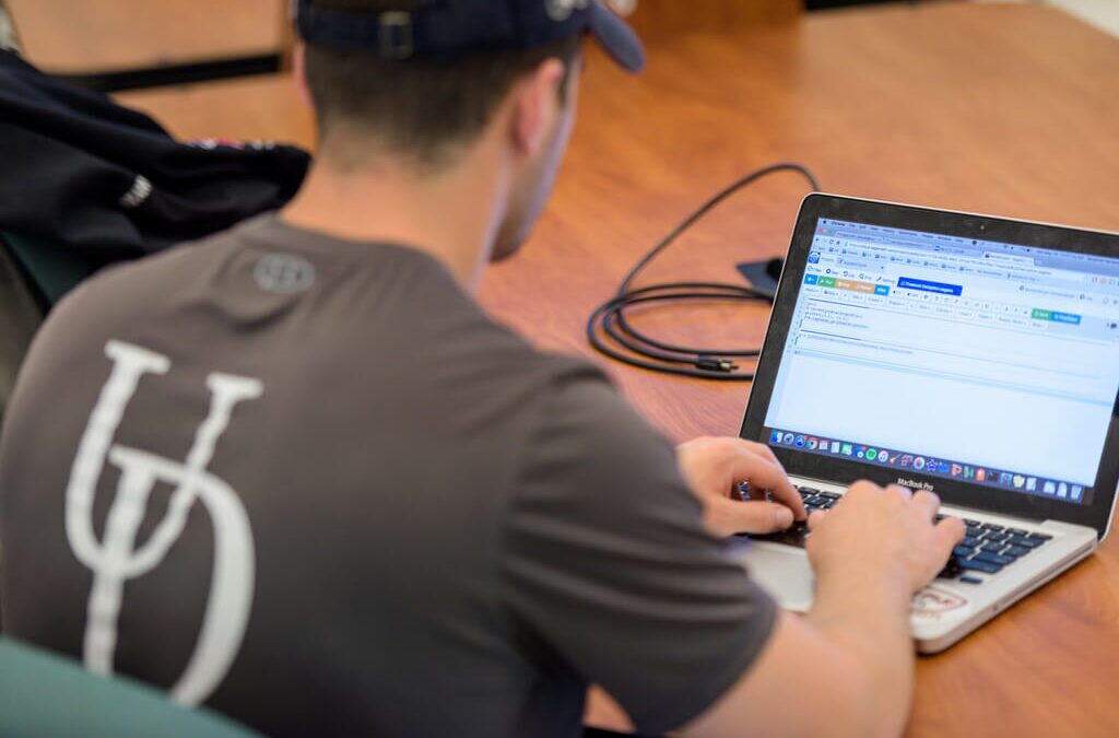 Student in t-shirt with UD logo looking at a laptop screen.