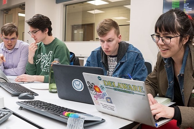 Students and a professor work on cybersecurity problems on laptops