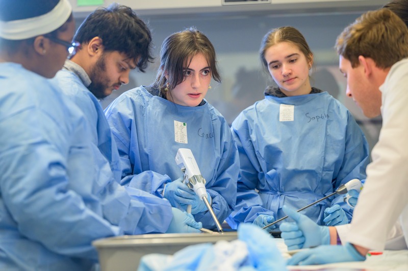 Students use a surgical stapler under the instruction of J&J MedTech sales training representative Coln Raad (right, white coat).