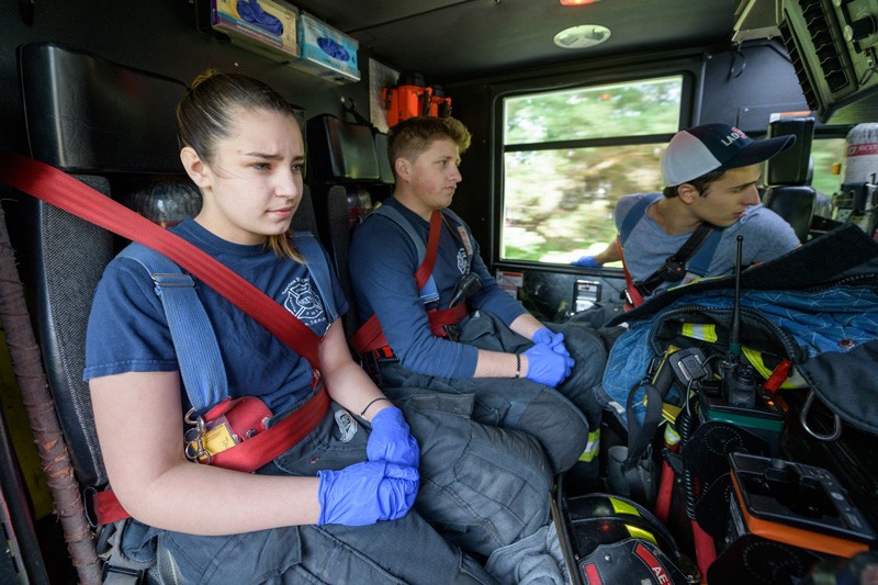 Olivia Alexander (left), Connor Sproat (middle) and Matthew Heebner are UD students who volunteer with the Aetna fire station. With the concentration evident on their faces, the three ride in the back of the truck to the scene of a recent emergency call. 