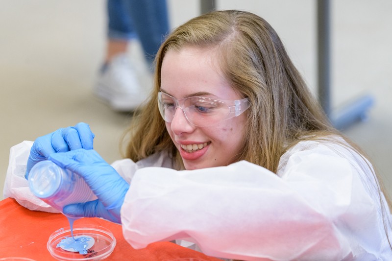 student pours a substance into a Petri dish