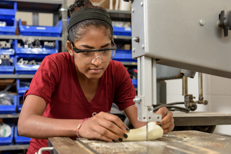 A female student uses a band saw to cut a simulated piece of bone